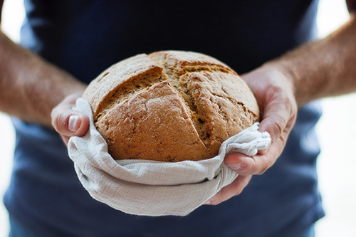 hands holding artisan loaf of bread in tea towel