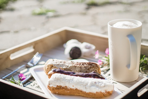 Chocolate, raspberry, and coconut eclairs on tray with coffee